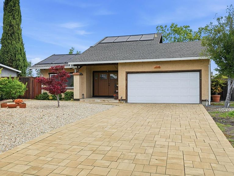 The front elevation of 4002 Agatha Way: paver driveway, Japanese maple, solar panels on the roof, and a two-car garage with a clean modern facade
