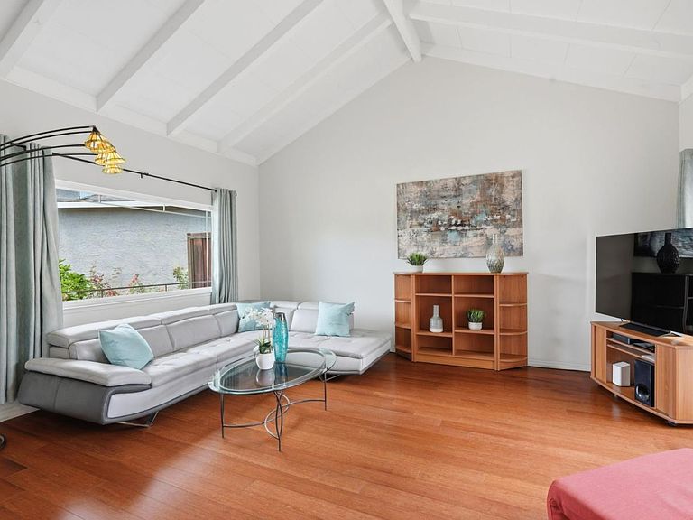 The vaulted-ceiling great room with exposed white beams, hardwood floors, and a picture window looking onto the side yard