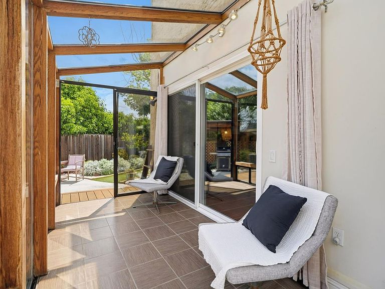 The glass-roofed sun room atrium with timber framing, sliding glass doors opening onto a garden patio, and views toward the backyard